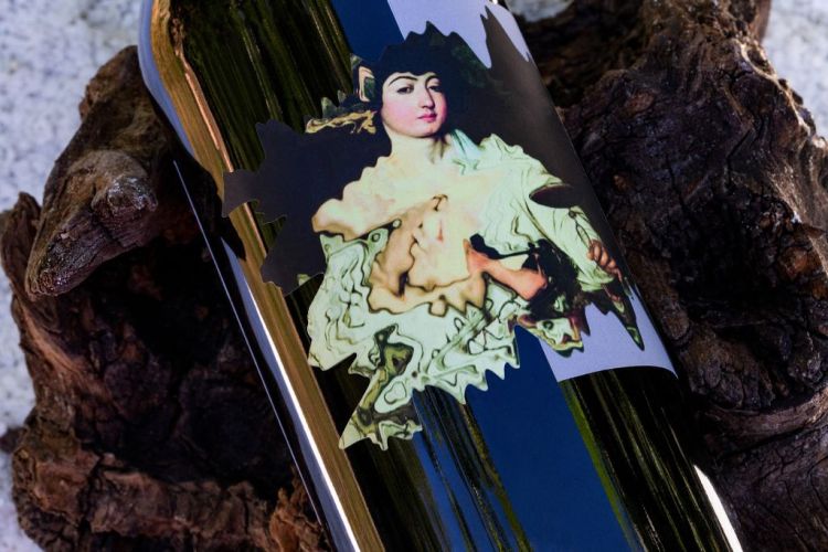 Closeup of a shiny dark wine bottle with a painting of a woman on the label against a wood pedestal
