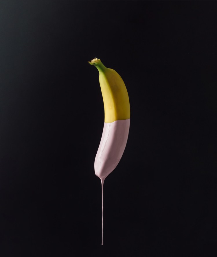 Banana with dripping pink paint on dark background